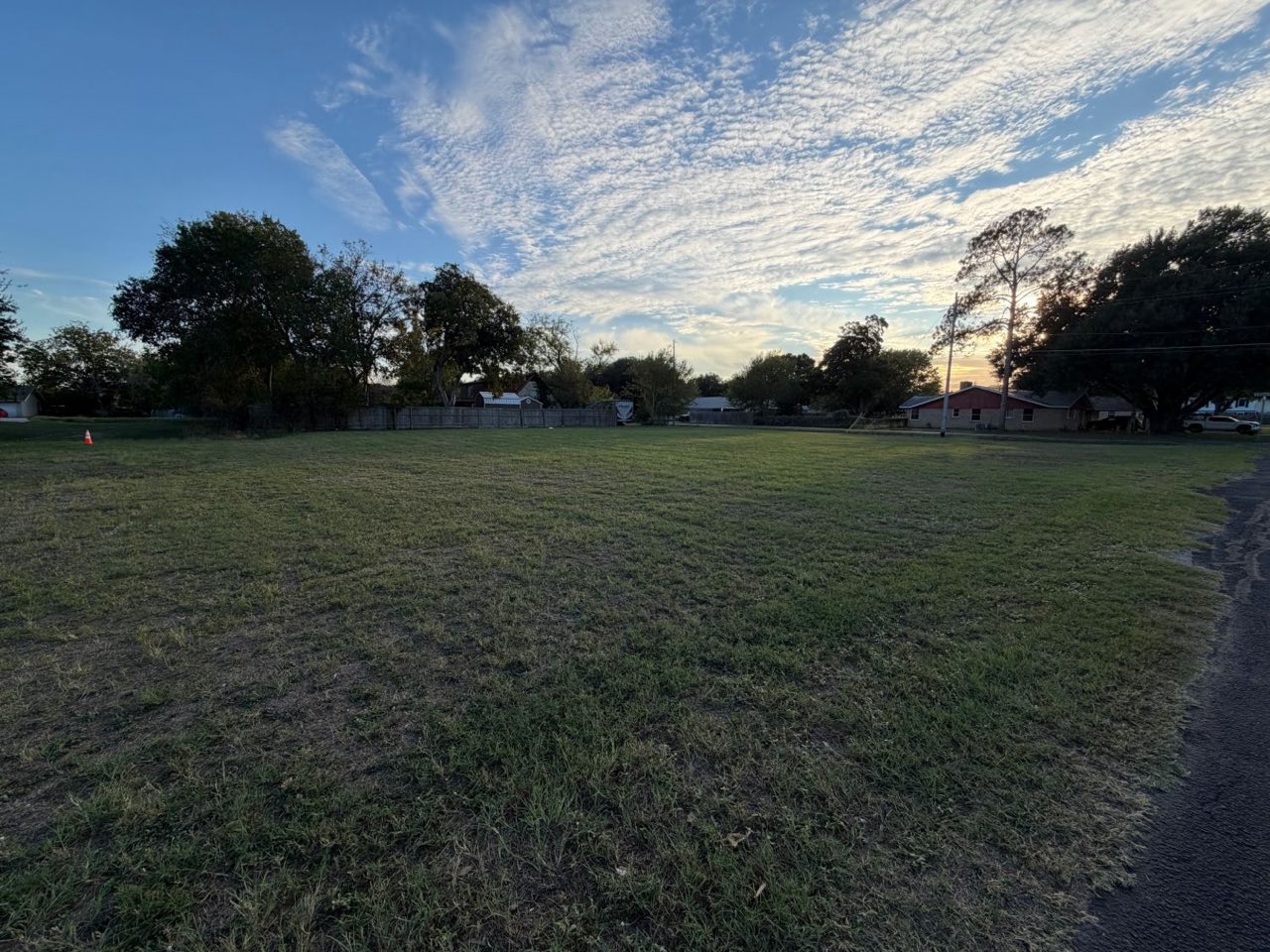Open grass lot at sunset with the street along the right edge