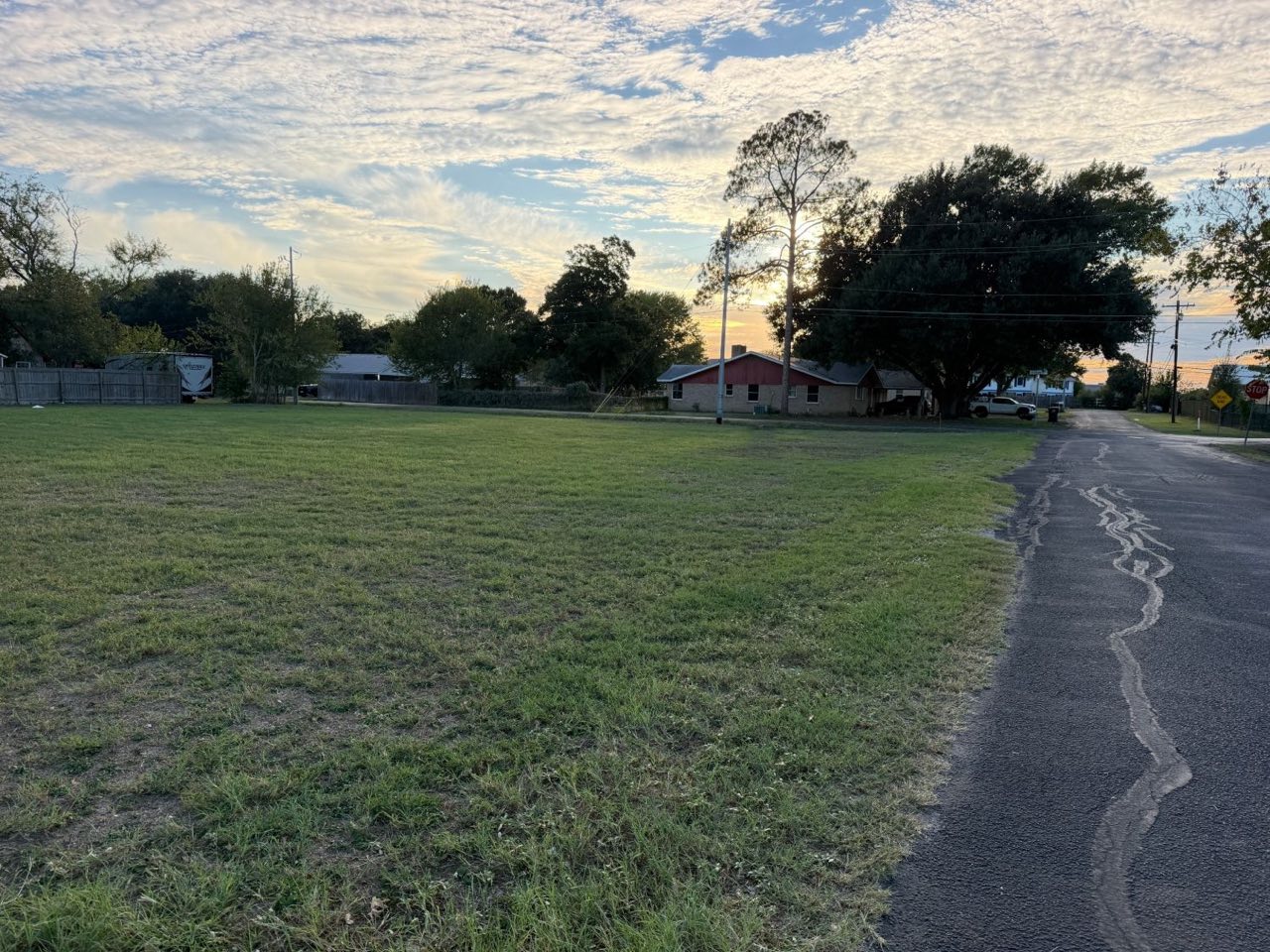 Level grass lot with the street on the right and neighboring homes beyond
